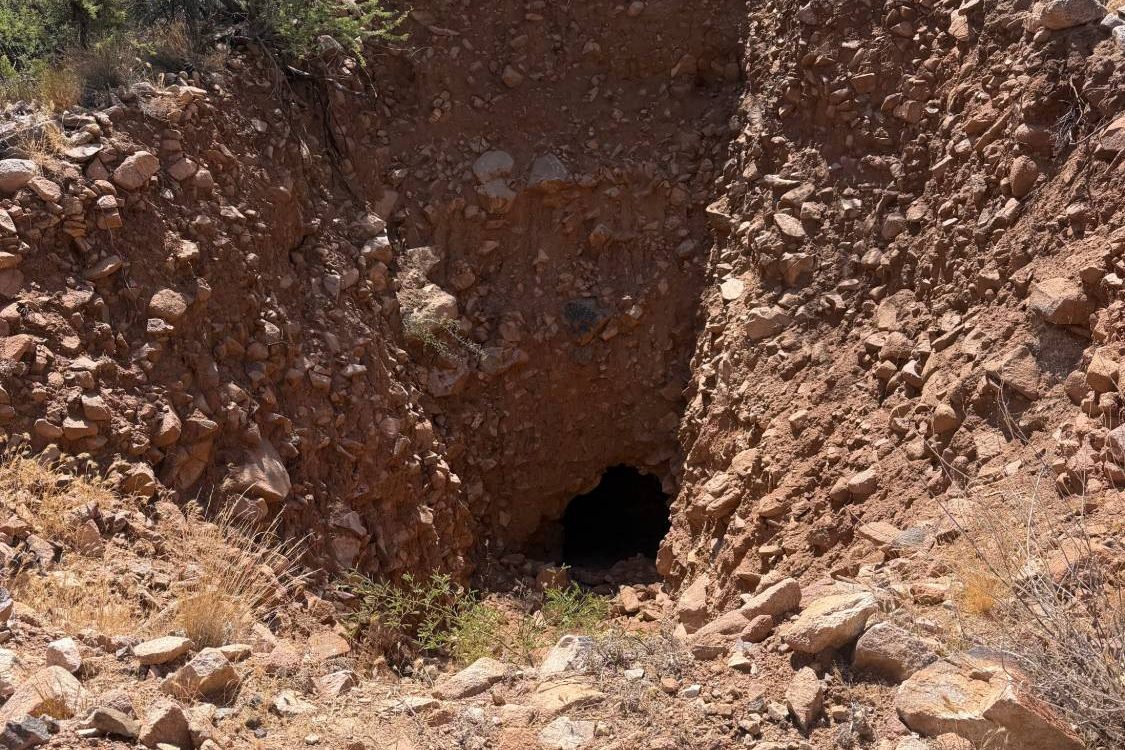 The dark opening of an old mine working at the back of a prospect cut in red Arizona rock